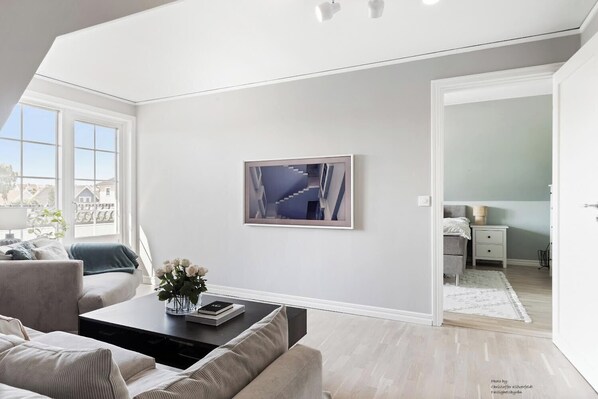 A modern living room with a large window, a painting, and a view of the outside.