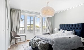A bedroom with a large bed, a chair, a round light fixture, and a view through the window.