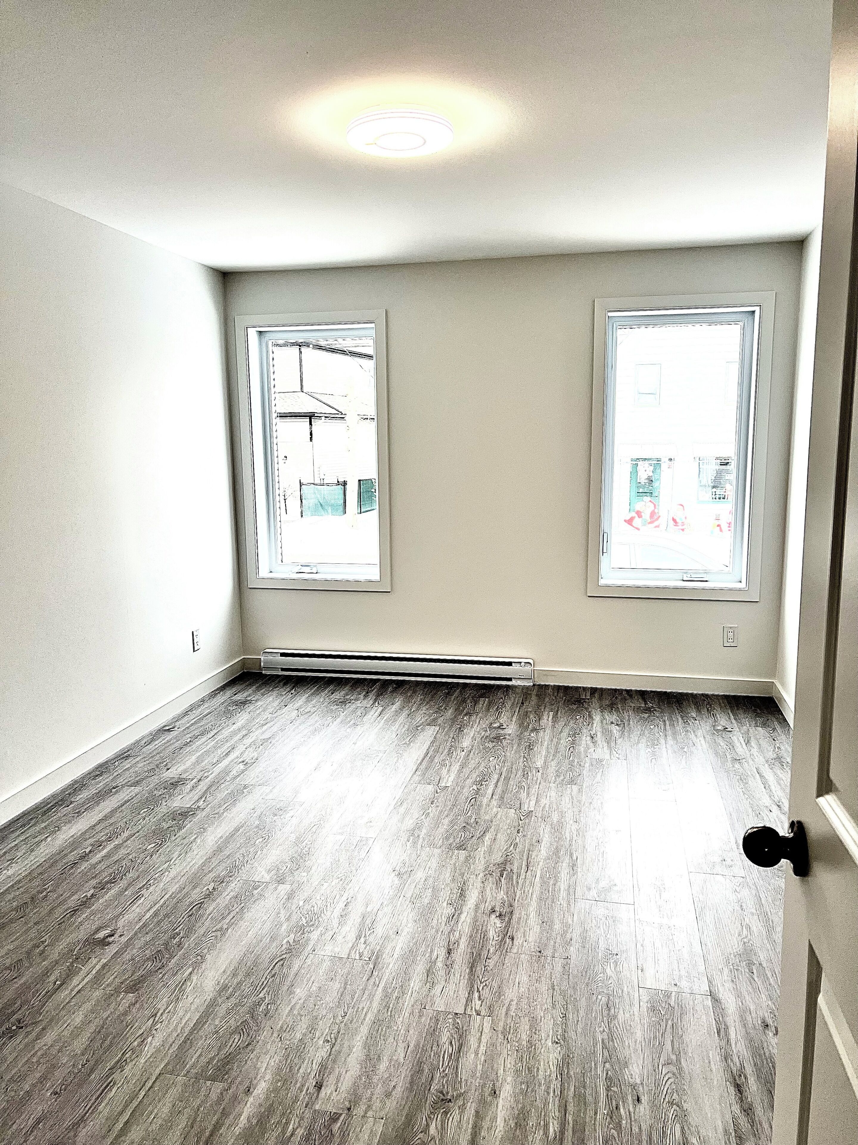 A room with two windows, a visible heating vent, and a hardwood floor.