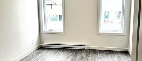 A room with two windows, a visible heating vent, and a hardwood floor.