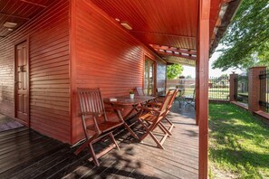 A covered outdoor patio with a wooden table and chairs, a door, and a view of a fenced area. - Two-story Holiday Home With a Terrace (Darlowo)