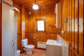 A wooden-paneled bathroom with a toilet, a window, a radiator, and a sink. - Two-story Holiday Home With a Terrace (Darlowo)