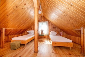A wooden attic bedroom with two beds, a chair, and a small table. - Two-story Holiday Home With a Terrace (Darlowo)