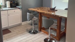 A kitchen with a wooden table and bar stools, a microwave, and a window with blinds.