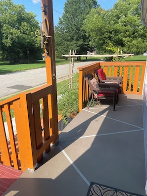 A wooden deck with a chair and a bench, a metal gate, and a view of a street and greenery.
