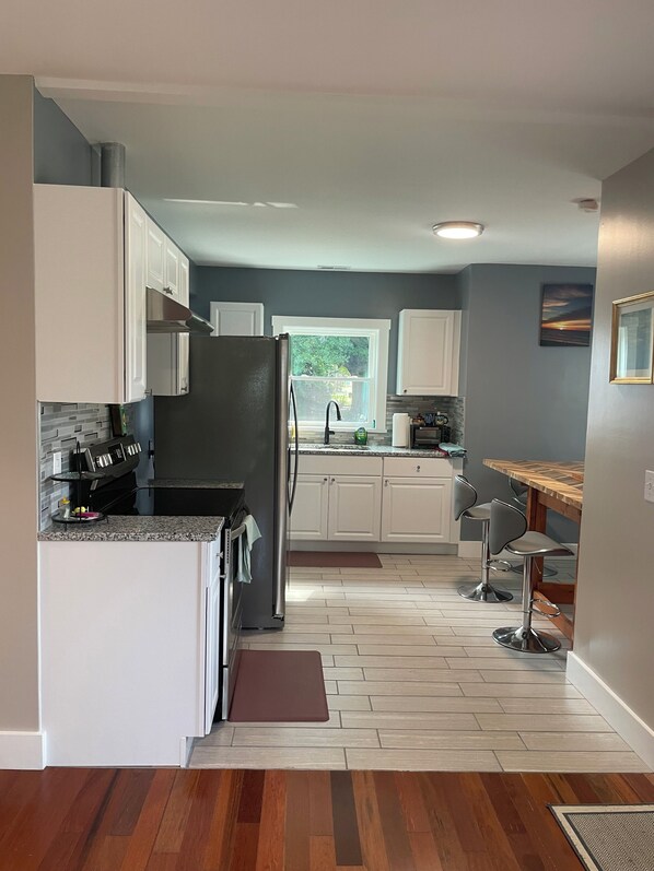 A modern kitchen with white cabinets, a black refrigerator, and a wooden dining table with two chairs.