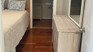 A bedroom with a bed, a dresser, a mirror, and a walk-in closet.