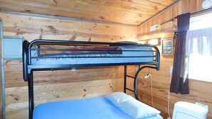 Ein Etagenbett mit blauer Matratze und weißem Kopfkissen in einem Holzhütten-Schlafraum.