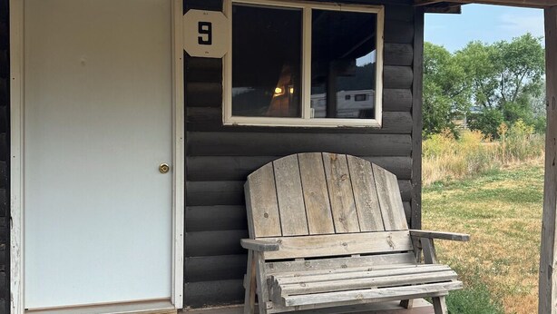 Eine Blockhütte mit Veranda, einem Holzstuhl und einer Tür, auf der die Nummer 9 steht.
