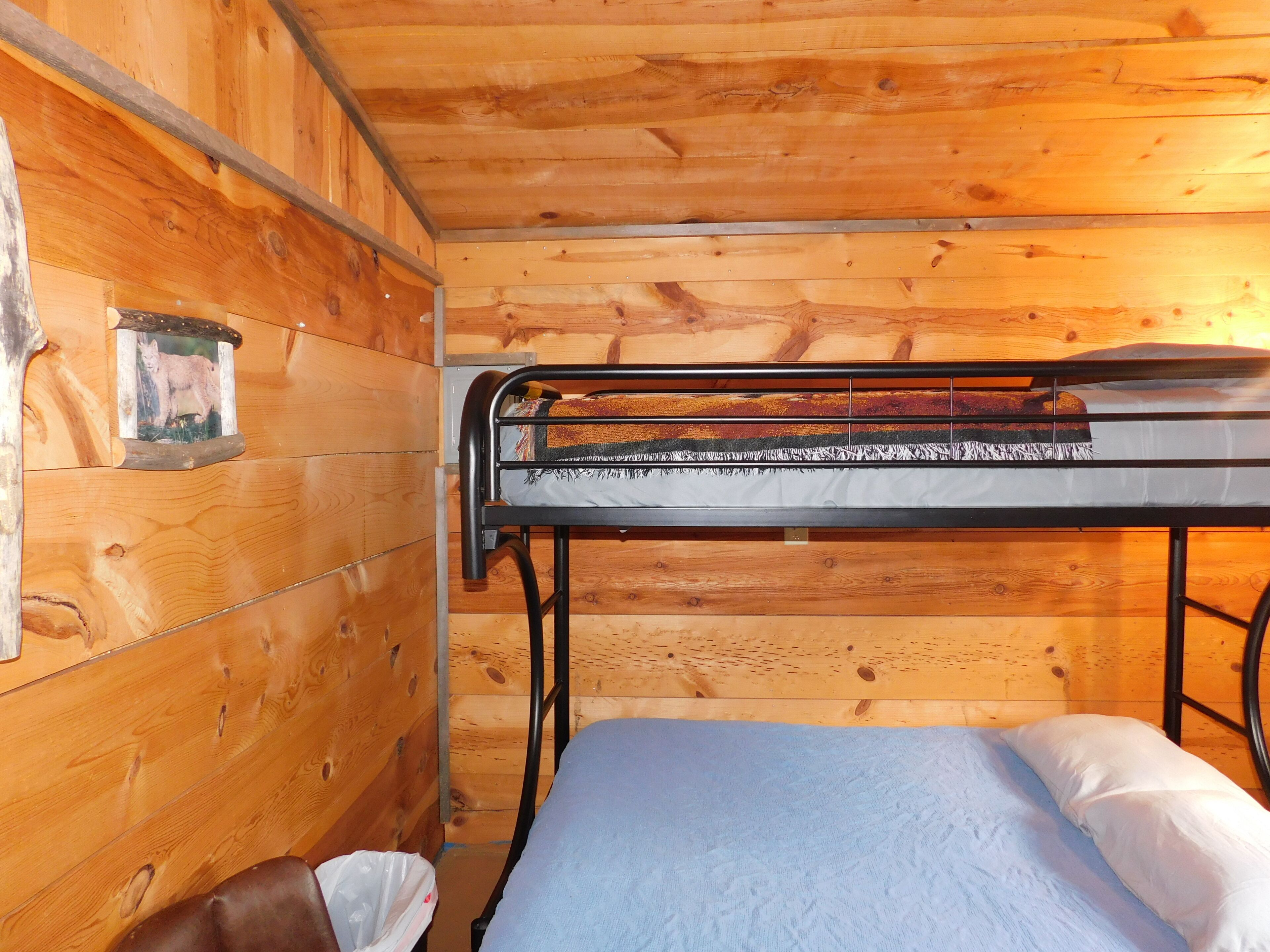 A bunk bed with a metal frame and a single mattress, a wooden wall with a picture frame, and a brown leather chair.