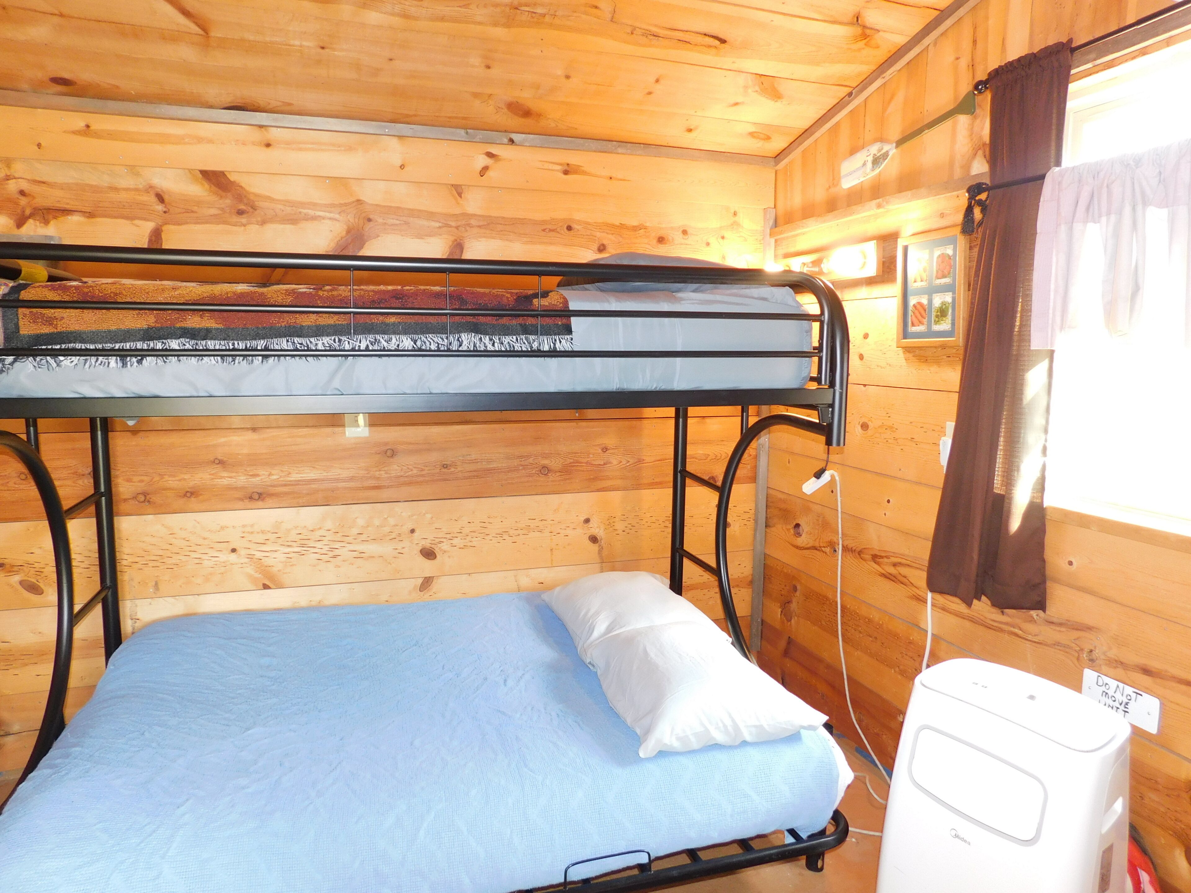 A bunk bed with a mattress and pillows, a white heater, and wooden walls.
