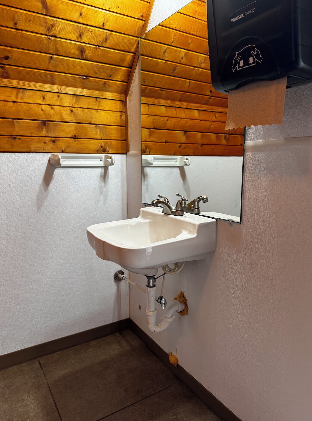 A bathroom with a white sink, a mirror, and wooden ceiling.
