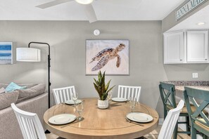 Ein Essbereich mit einem runden Tisch, weißen Stühlen und einem Gemälde einer Schildkröte an der Wand.