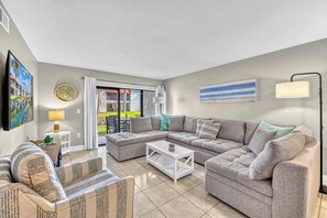 Ein Wohnzimmer mit einer Eckcouch, einem Couchtisch, einem Fernseher und einem Gemälde an der Wand.