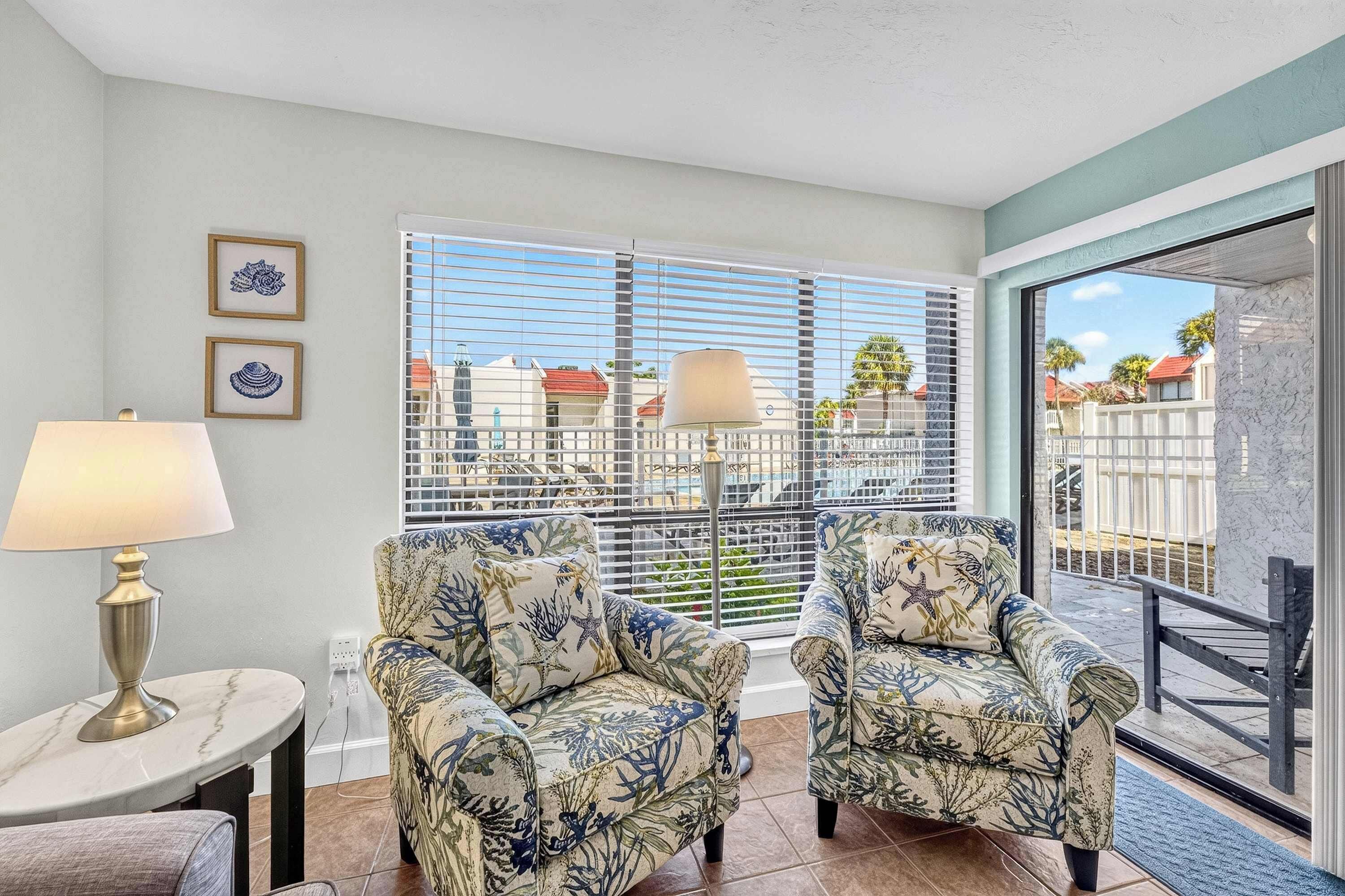 A room with two armchairs, a table, and a lamp. There are two framed pictures on the wall.