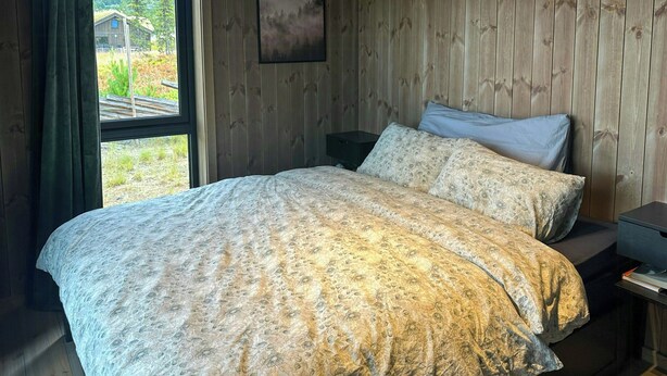 Une chambre à coucher avec un lit, des murs en bois, une fenêtre et une table de chevet.