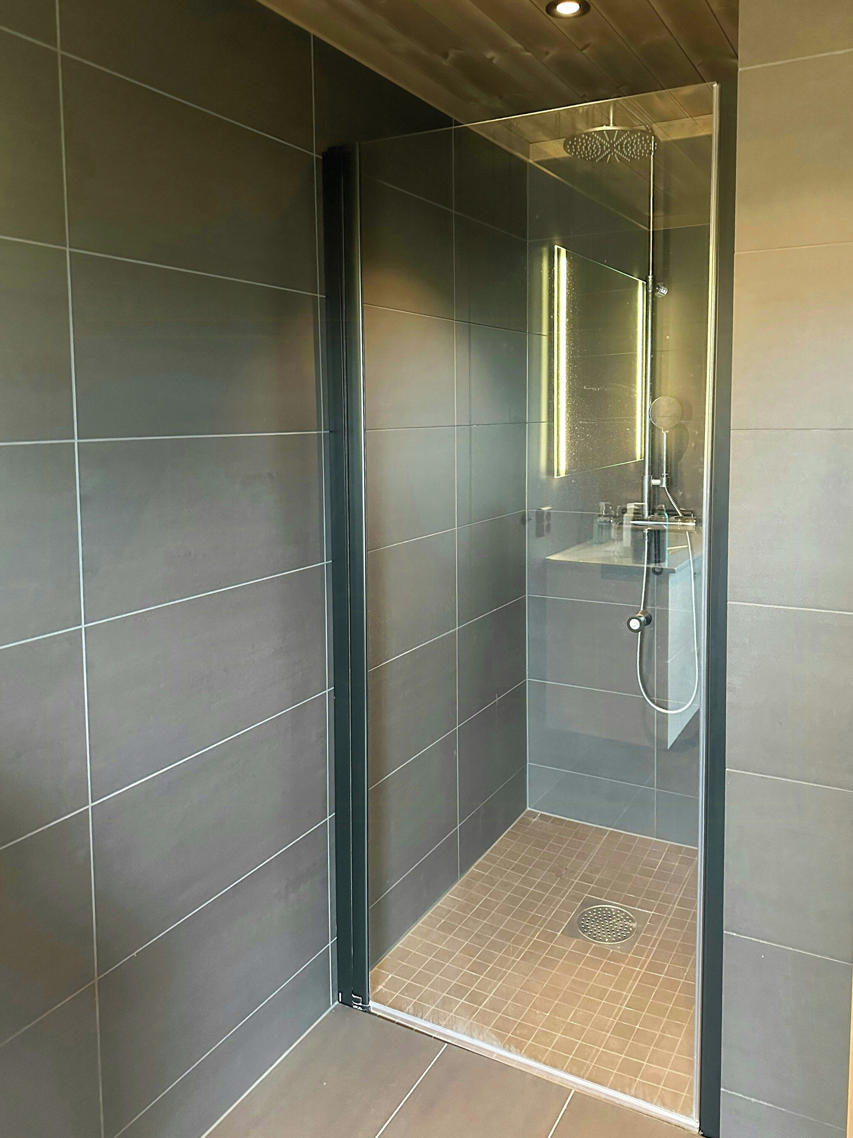 Un box de ducha moderno con puerta de cristal, un cabezal de ducha de mano y un panel de control visible.