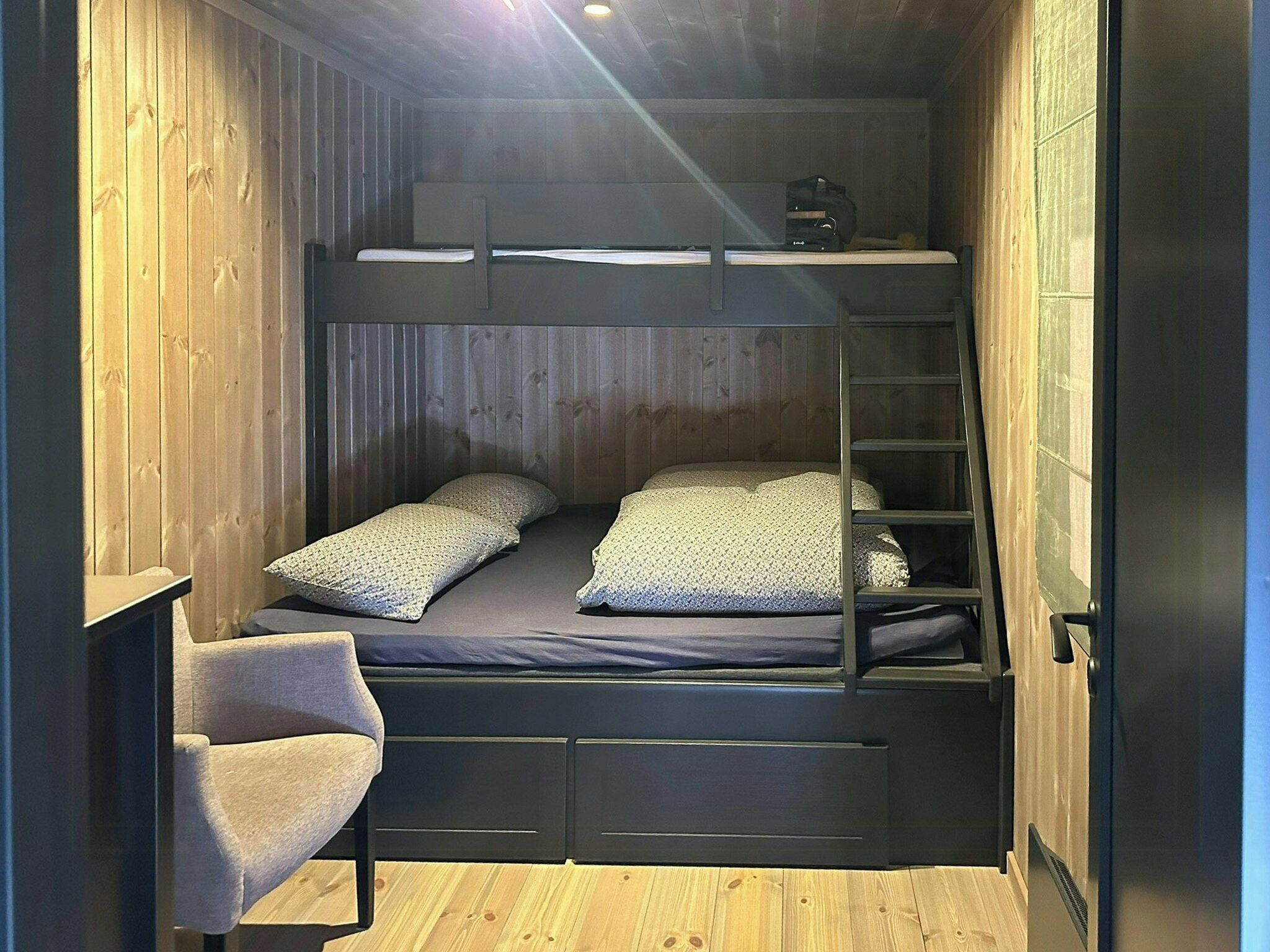 A bunk bed with a desk and chair, wooden walls, and a ladder.