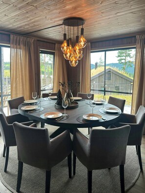 A dining area with a round table set for six, surrounded by chairs, and a modern chandelier above. - Sunny retreat on Nesfjellet near alpine skiing (Buskerud)