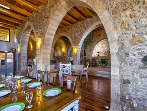 A dining area with a wooden table set for a meal, stone arches, and a stone wall. - Villa Candice With Private Pool (Rethymno)