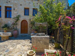 A stone building with a wooden door and windows, surrounded by potted plants and a stone fountain. - Villa Candice With Private Pool (Rethymno)