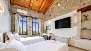 A hotel room with two beds, a TV, stone walls, and a wooden ceiling. - Villa Candice With Private Pool (Rethymno)