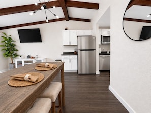 Una cocina moderna con una mesa de comedor de madera preparada para dos personas, un refrigerador de acero inoxidable y un televisor de pantalla plana montado en la pared.