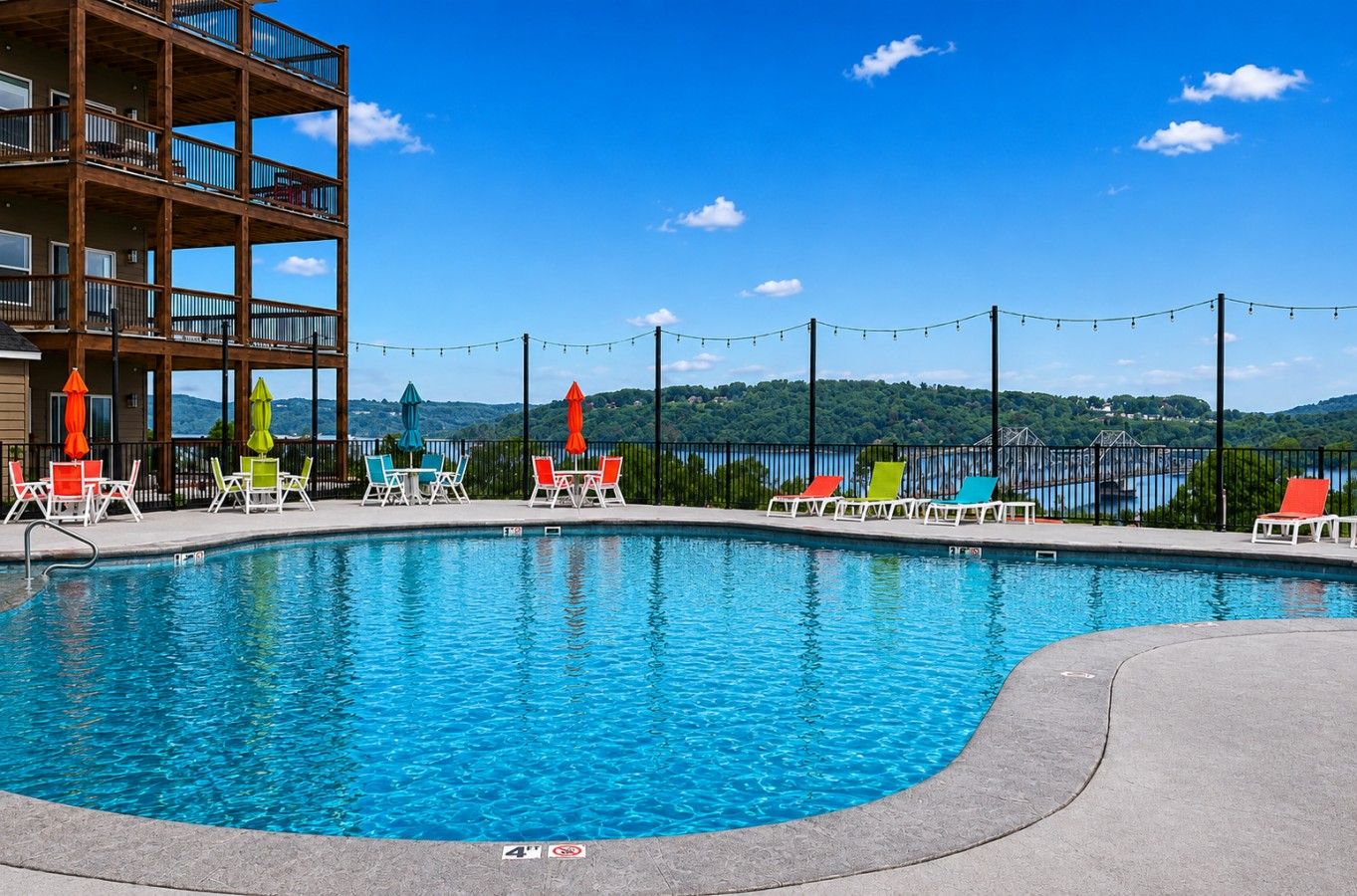 A swimming pool with lounge chairs and umbrellas, surrounded by a building with balconies.