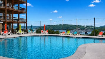 A swimming pool with lounge chairs and umbrellas, surrounded by a building with balconies.