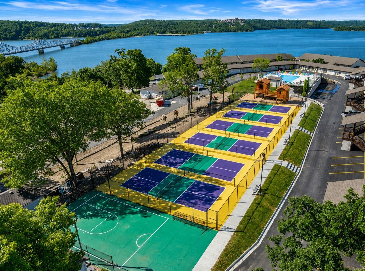 Ein Mehrsporthof mit Basketball- und Tennisplätzen, umgeben von Bäumen und Blick auf einen See.