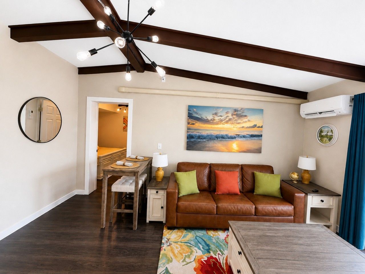 A living room with a brown leather sofa, a dining table, and a painting of a sunset.