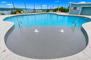 Una piscina con zona de hidromasaje, sillas de descanso y vistas a las colinas.