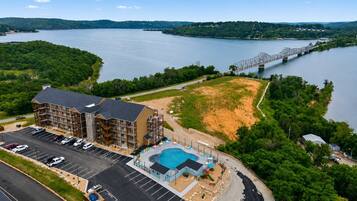 A multi-story hotel with a swimming pool, parking lot, and a view of a lake and bridge.