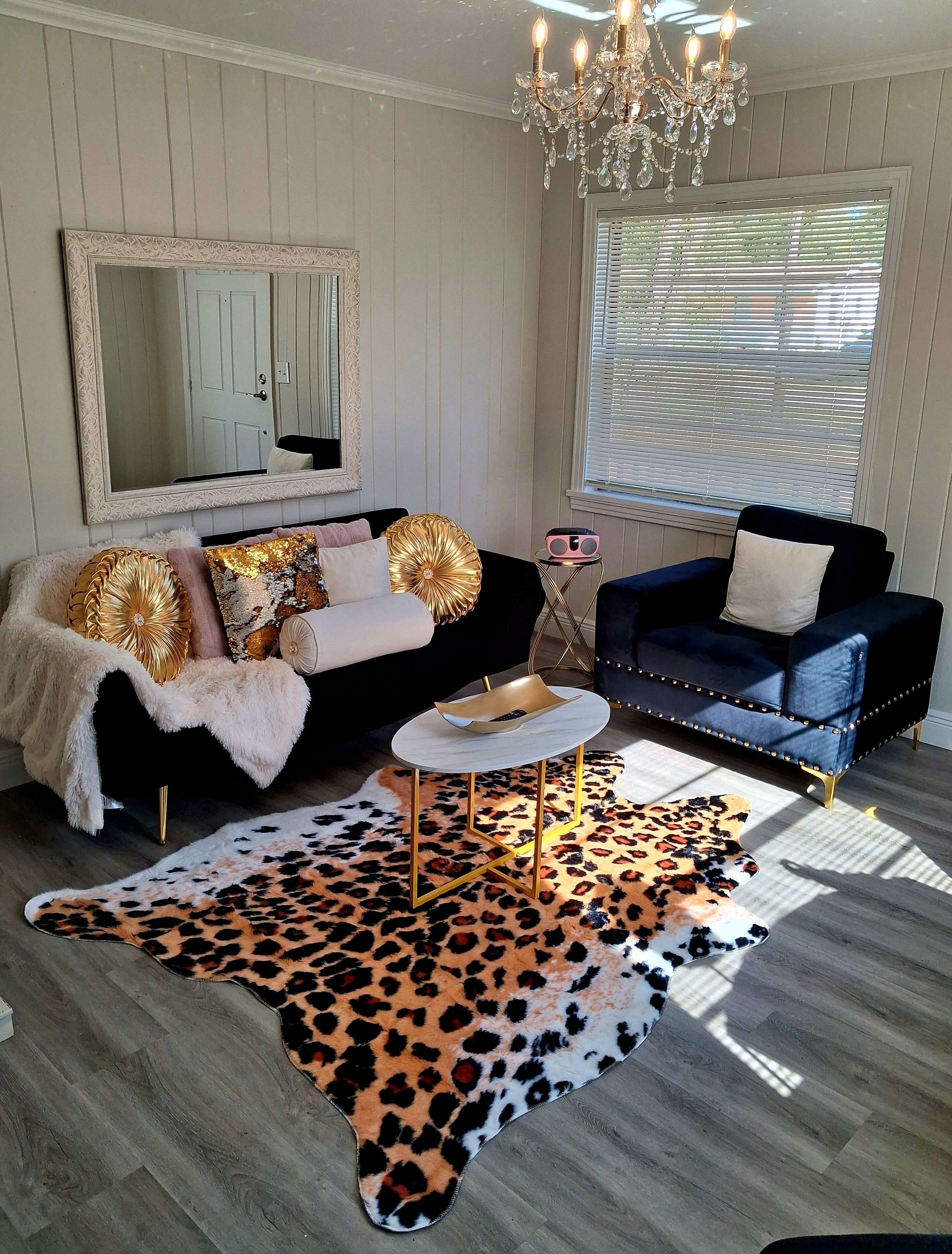 Un salon avec un canapé noir et blanc, un fauteuil bleu, un tapis à motifs léopard, une table basse ronde et un lustre.