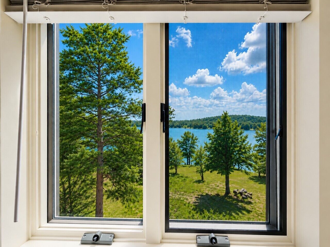 A window with a view of a lake, trees, and a clear sky.