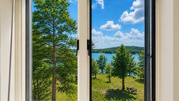 A window with a view of a lake, trees, and a clear sky.