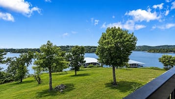Udsigt over en sø med træer, en græsplæne og en bygning med hvidt tag.