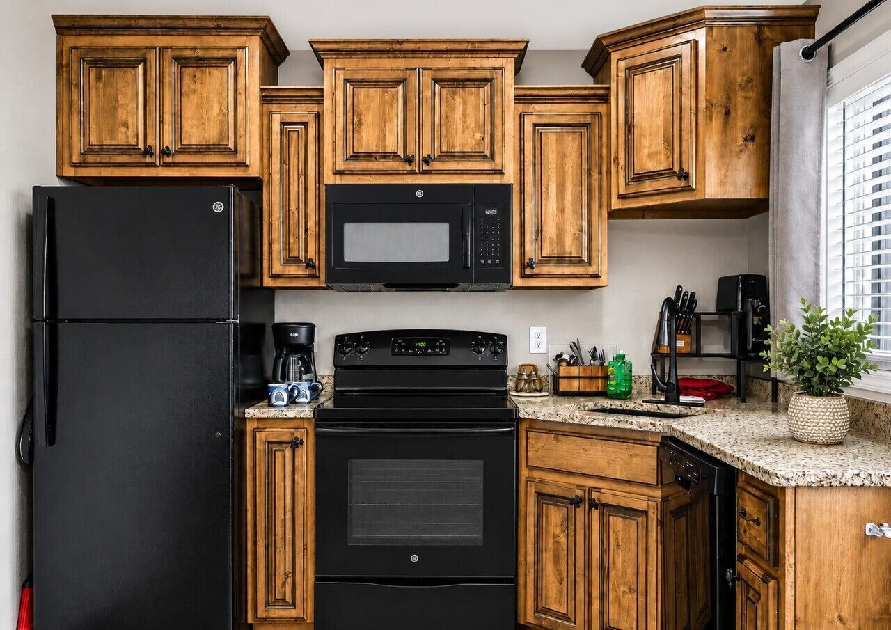 A kitchen with wooden cabinets, a black refrigerator, a microwave, a stove, and a coffee maker.