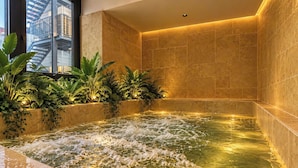 Un espace bien-être comprenant un jacuzzi, des murs carrelés et des plantes d’intérieur.