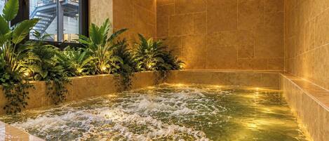 Uma área de spa com hidromassagem, paredes revestidas de azulejos e plantas.