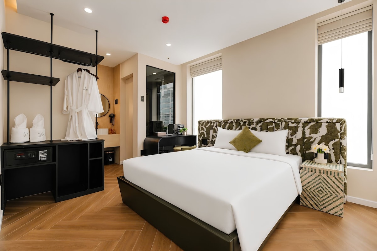 A modern hotel room with a large bed, a desk, a wardrobe, and a bathroom visible through an open door.
