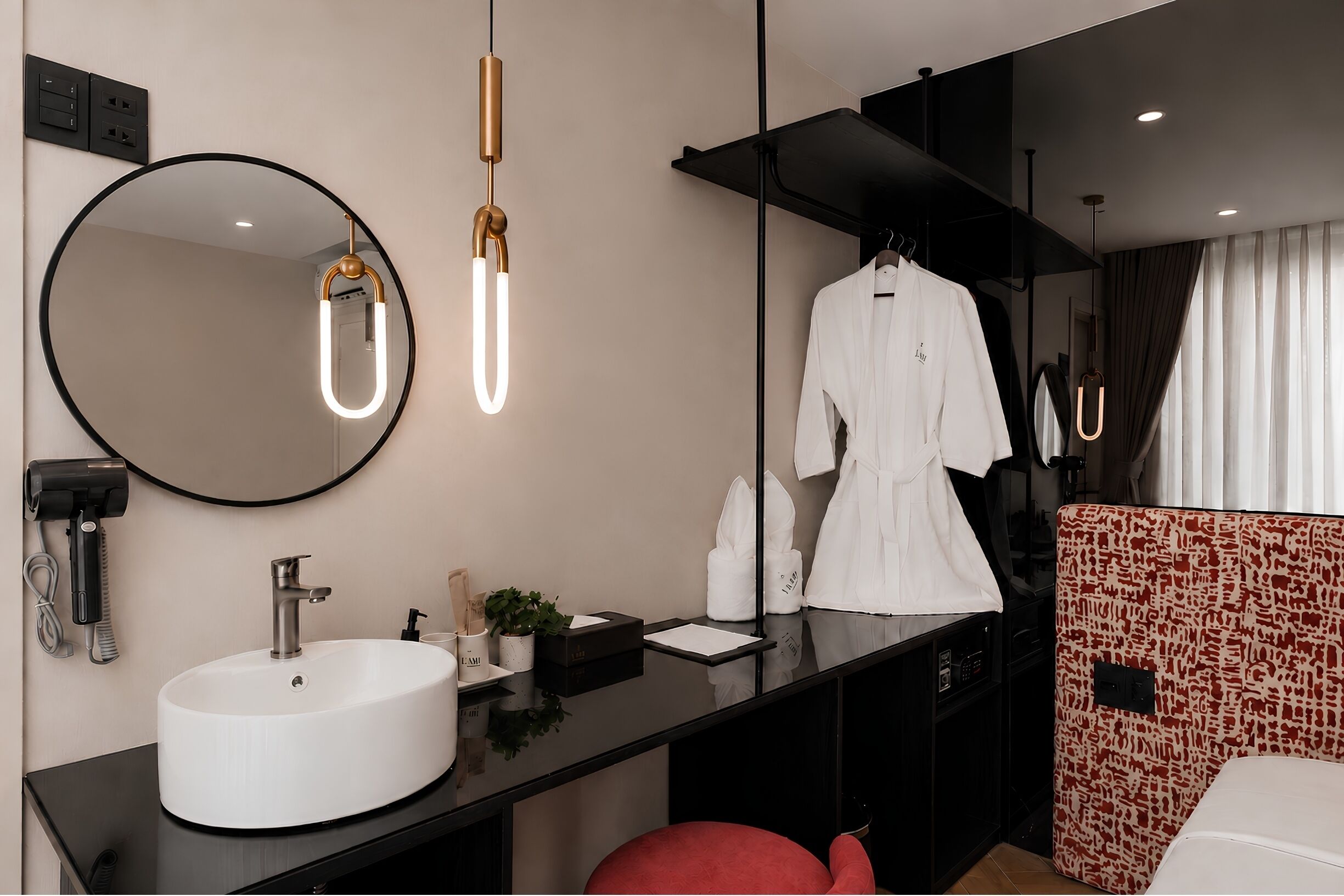 Une salle de bain moderne avec un miroir rond, un lavabo blanc, une robe suspendue à un porte-manteau et une chaise rouge.
