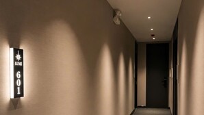 Un couloir avec une pancarte indiquant le numéro de la chambre 601, un plafond doté d’un éclairage encastré et une porte au bout du couloir.