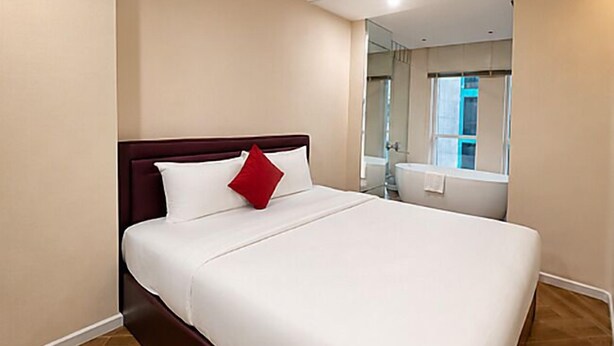 Une chambre d’hôtel avec un grand lit, un oreiller rouge, une fenêtre et une salle de bain visible à travers la porte.