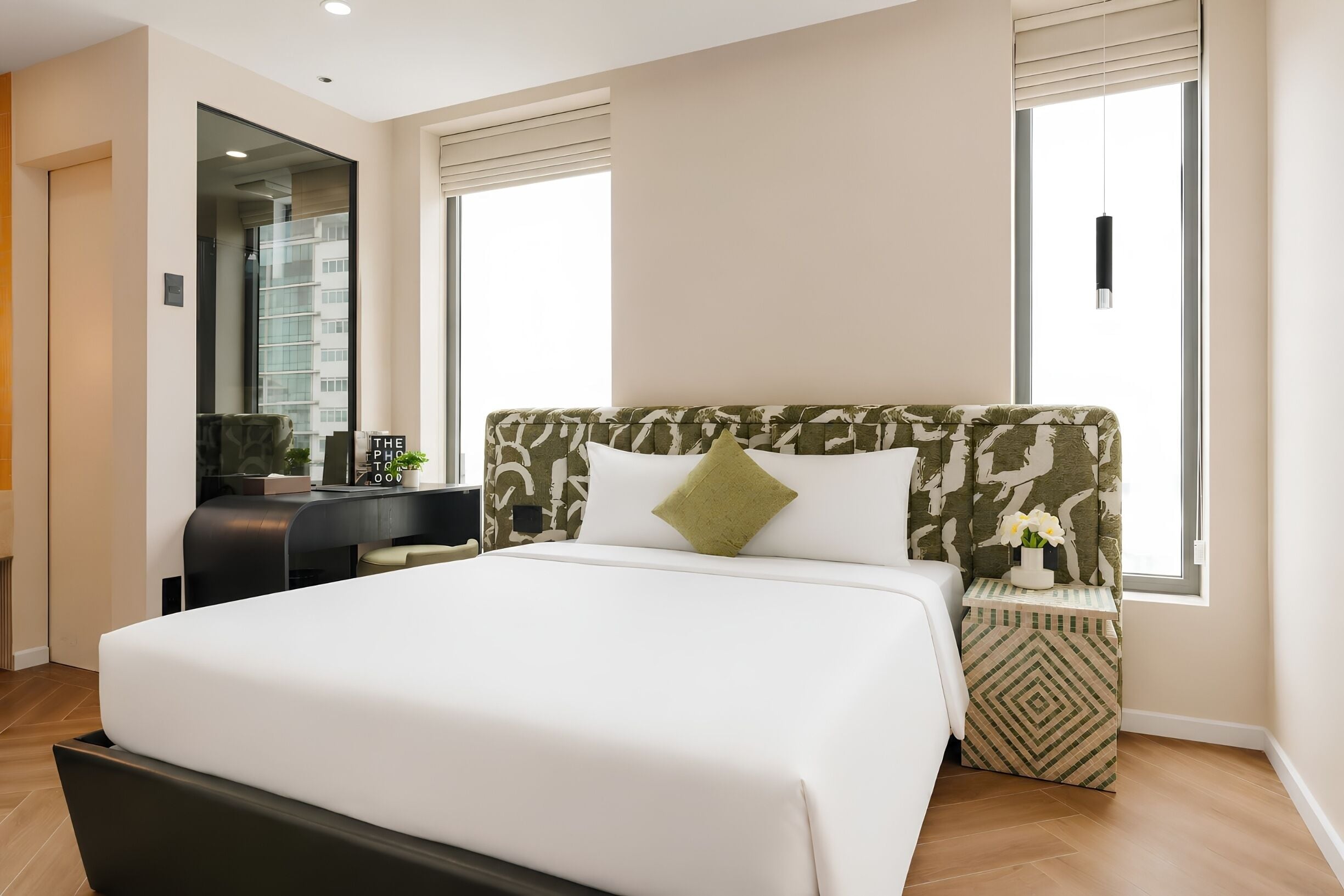 A modern hotel room with a large bed, a desk, and a window with blinds.