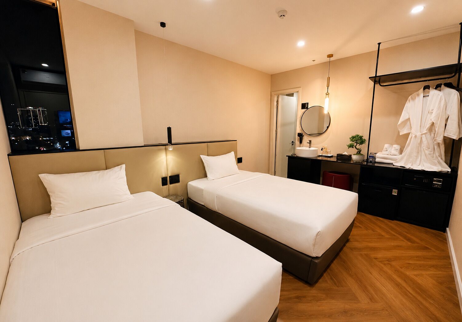 A hotel room with two beds, a bedside table, a mirror, a sink, and a robe rack.