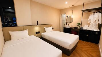 A hotel room with two beds, a bedside table, a mirror, a sink, and a robe rack.