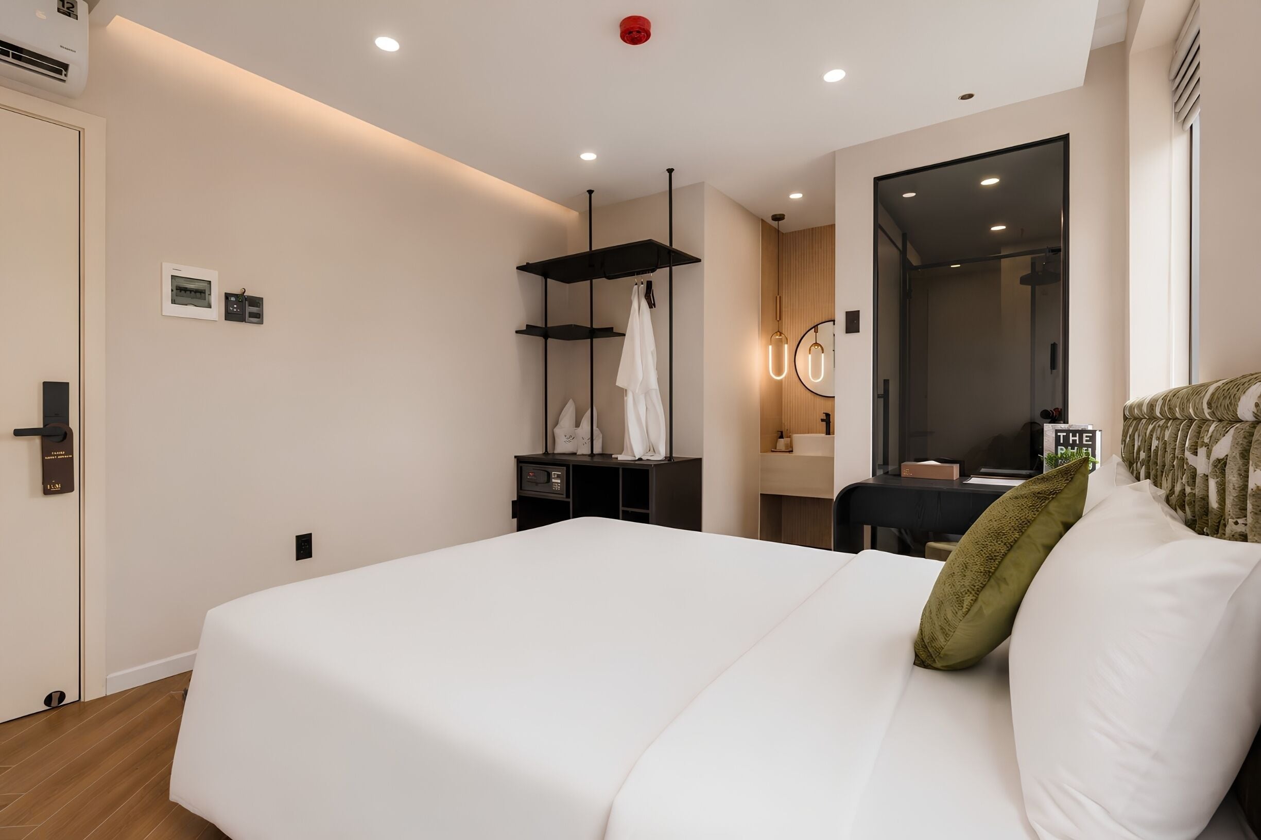 A hotel room with a large bed, a desk with a chair, a wardrobe, a mirror, and a bathroom visible through an open door.
