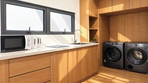 Une cuisine compacte équipée d’un four à micro-ondes, d’une bouilloire et d’un évier, ainsi que d’un lave-linge encastré.