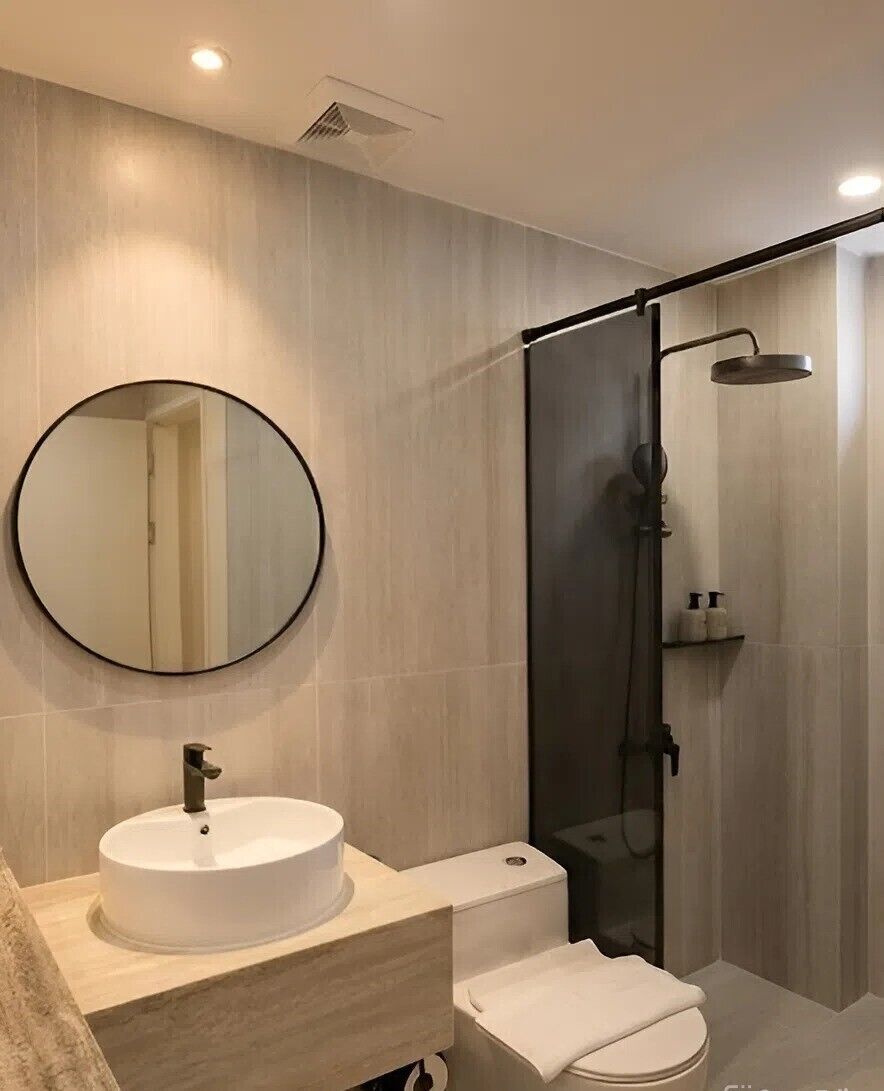 A modern bathroom with a round mirror, a sink, a toilet, and a glass-enclosed shower.